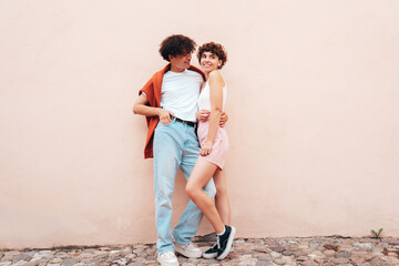 Young smiling beautiful woman and her handsome boyfriend in casual summer clothes. Happy cheerful family. Female having fun. Couple posing in street at sunny day. Near  wall. Having tender moments