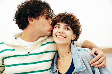 Smiling beautiful woman and her handsome boyfriend with curls hairstyle. Happy cheerful family having tender moments in white interior in studio.Pure cheerful models hugging. Kiss