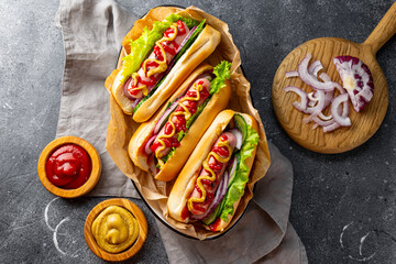 Homemade hot dogs with sausage, green salad, cucumber and red onion on the grey background top view