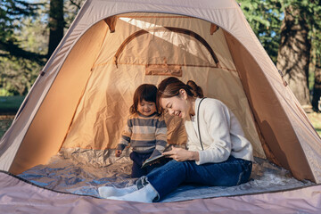 テントの中で娘に本を読み聞かせる母親