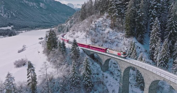 Landwasser Viaduct world heritage sight with luxury Glacier and Bernina express in Swiss Alps snow winter scenery. Aerial Drone shot red train passing through famous mountain in Filisur, Switzerland.