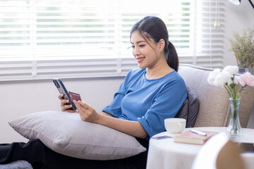 Obraz na płótnie Canvas Mobile Shopping. Cheerful Asian Woman Using Smartphone Shopping Online Holding Credit Card Making Payment Sitting At Sofa At Home. Internet Banking Application And E-Commerce 