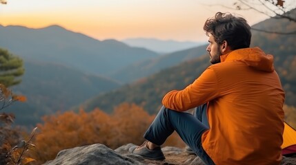 Lonely man enjoys the view of the autumn mountains while sitting in a tent. Hiking and digital detox concept. Contemplation of nature alone with your thoughts. Peace and slow life.