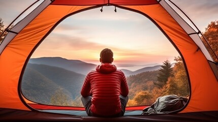 A man enjoys the view of the autumn mountains while sitting in a tent. Hiking and digital detox concept. Contemplation of nature alone with your thoughts. Peace and slow life. Alone with yourself - obrazy, fototapety, plakaty