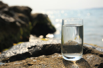 Glass of fresh water on stone near sea, space for text