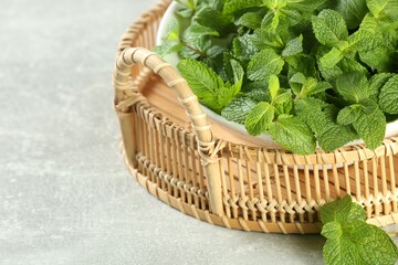 Fototapeta na wymiar Wicker tray with bowl of fresh green mint leaves on grey table, closeup. Space for text