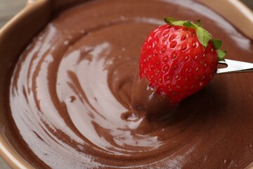Dipping strawberry into fondue with melted chocolate, closeup. Space for text
