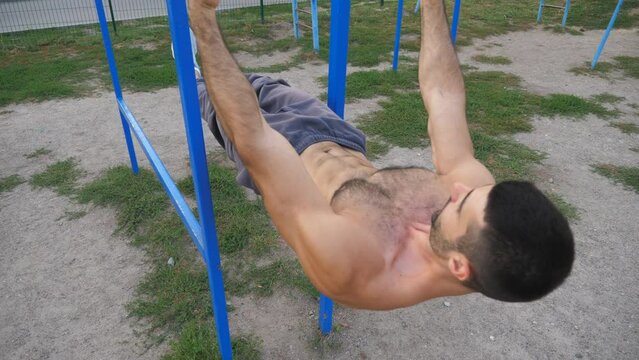 Muscular sportsman doing showing some gymnastics tricks on parallel bars at sports ground. Young athlete performing static exercises during workout outdoor. Concept of sportive lifestyle. Dolly shot