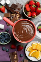 Fondue pot with melted chocolate, marshmallows, fresh orange and different berries on grey table, flat lay