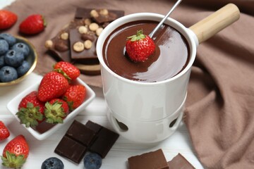 Dipping fresh strawberry in fondue pot with melted chocolate at white wooden table