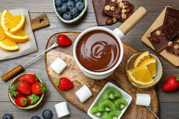 Flat lay composition with fondue pot of melted chocolate on wooden table