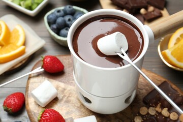 Dipping sweet marshmallow in fondue pot with melted chocolate at wooden table