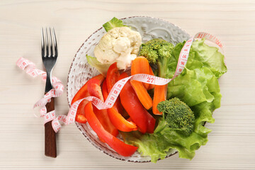 Healthy diet. Plate of fresh vegetables, measuring tape and fork on light wooden table, top view