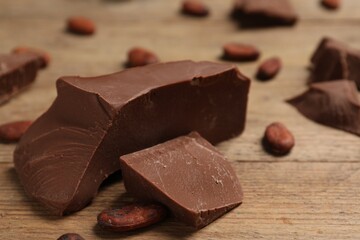 Pieces of tasty milk chocolate and cocoa beans on wooden table, closeup