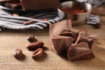 Pieces of tasty milk chocolate and cocoa beans on wooden table, closeup