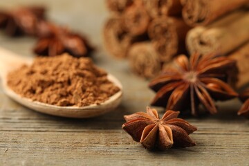 Spoon with cinnamon powder, sticks and star anise on wooden table, closeup