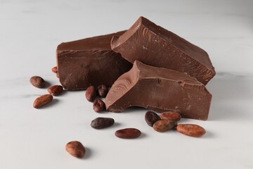 Pieces of tasty milk chocolate and cocoa beans on white marble table, closeup