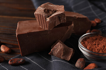 Pieces of tasty milk chocolate and cocoa beans on table, closeup