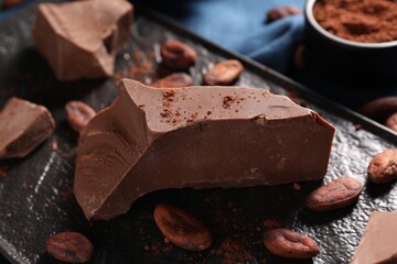 Pieces of tasty milk chocolate and cocoa beans on table, closeup