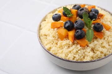 Bowl of tasty couscous with blueberries, pumpkin and mint on white table, closeup. Space for text