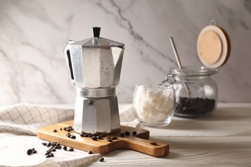 Moka pot and coffee beans on white wooden table, space for text
