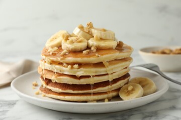 Fototapeta na wymiar Delicious pancakes with bananas, walnuts and honey on white marble table, closeup