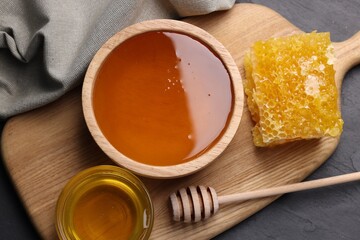 Sweet honey in bowls, dipper and pieces of honeycomb on grey table, flat lay