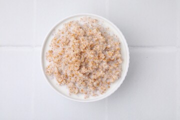 Tasty wheat porridge with milk in bowl on white table, top view