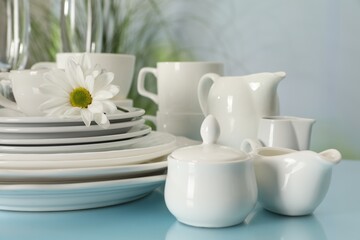 Fototapeta na wymiar Set of clean dishware and flower on light blue table, closeup
