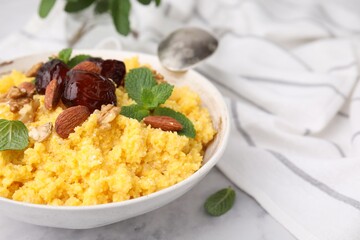 Tasty cornmeal with dates, nuts and mint in bowl on white table, closeup. Space for text