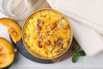 Tasty cornmeal with nuts, pumpkin and seeds in bowl served on white tiled table, flat lay
