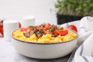 Tasty cornmeal with tomatoes, bacon and microgreens in bowl on white table, closeup