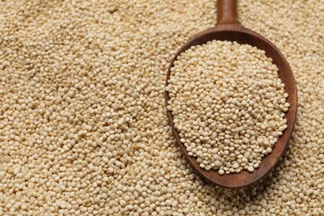 Wooden spoon and raw quinoa as background, closeup. Space for text