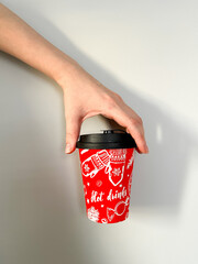 paper cup with a New Year's print, which is held by a girl's hand on a light background