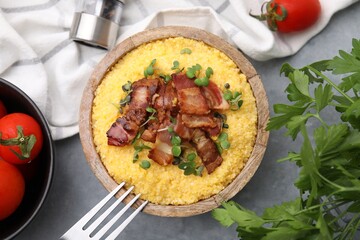 Cooked cornmeal with bacon and microgreens in bowl on light grey table, flat lay