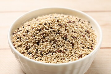 Raw quinoa seeds in bowl on table, closeup