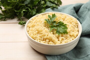 Delicious bulgur with parsley in bowl on wooden table, closeup. Space for text