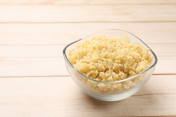 Delicious bulgur in glass bowl on wooden table, closeup. Space for text