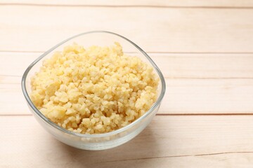 Delicious bulgur in glass bowl on wooden table, closeup. Space for text