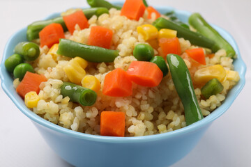 Delicious bulgur with vegetables in bowl on white table, closeup