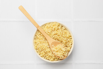 Delicious bulgur served on white tiled table, top view