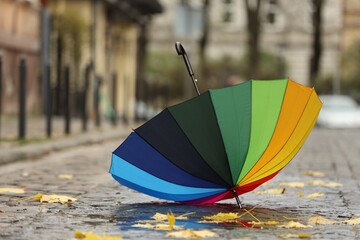Open colorful umbrella and fallen leaves on city street. Space for text