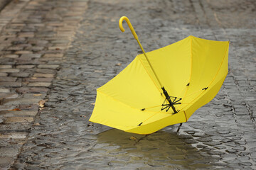 Open yellow umbrella on wet pavement. Space for text