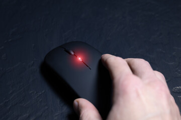 Black wireless minimalist mouse with mans hand on the black background. Modern technology device.