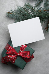 Fototapeta na wymiar White paper card mockup, blank christmas card with copy space for card design or text presentation, gift box with red bow and fir tree branch