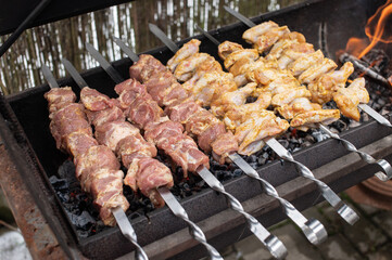 Shish kebab from different types of meat on skewers is fried on fire and coals in the grill