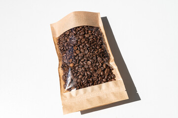 A kraft paper bag with coffee beans for viewing with a highlighted shadow on a white background.