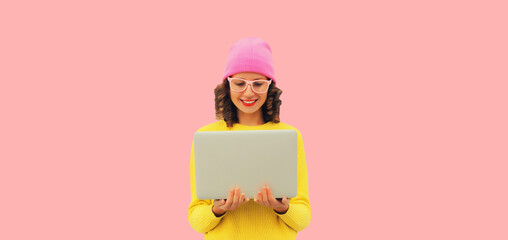 Stylish modern happy young woman working with laptop wearing colorful clothes, yellow sweater, hat...