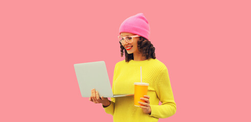 Stylish modern happy young woman working with laptop wearing colorful clothes, yellow sweater, hat...