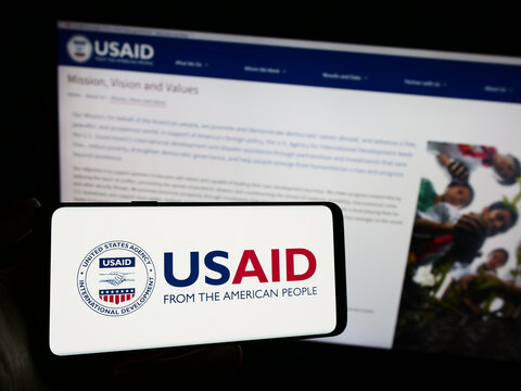 Stuttgart, Germany - 11-27-2023: Person holding mobile phone with logo of United States Agency for International Development (USAID) in front of web page. Focus on phone display.
